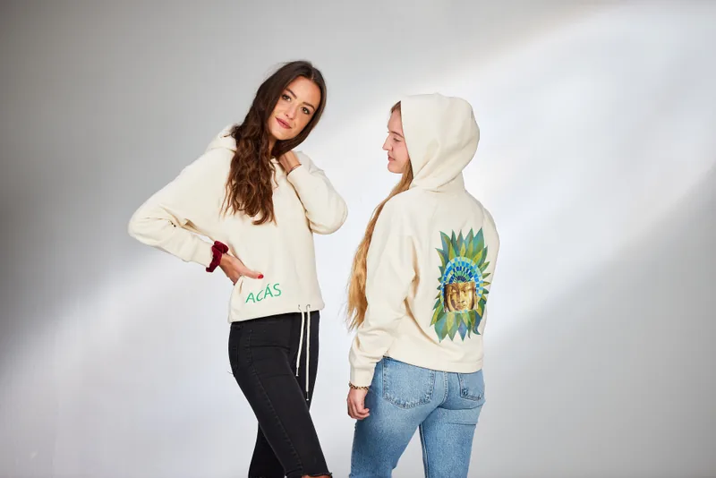 Zwei junge Frauen in cremefarbenen Hoodies, eine mit Bildmotiv am Rücken