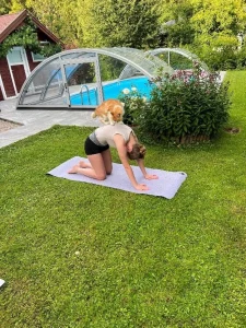 Frau bei einer Yogaübung auf einer Matte im Garten neben einem Pool