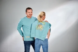 Mann und Frau in türkisen Sweatern, sie mit Bildmotiv am Rücken