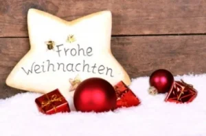 Stern mit der Aufschrift „Frohe Weihnachten“ und rote Christbaumkugeln im Schnee
