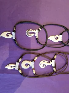 Weitere Maori-Anhänger aus Knochen an schwarzen Bändern auf violettem Tuch